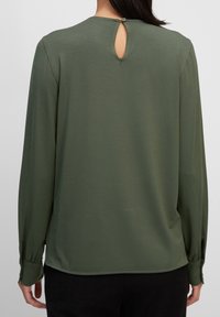Camicia verde a maniche lunghe in tessuto morbido, con apertura a chiave sul retro e chiusura con bottone, e polsini aderenti.