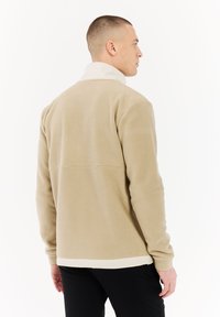 Beige fleece jack met een witte kraag, voorzien van een relaxed fit, lange mouwen en een soepele textuur. Opvallende stiksels over de rug.