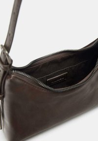Donkerbruin leren handtas met ritssluiting, voorzien van een binnenzak en een gladde textuur. Verstelbare schouderband voor veelzijdig dragen.