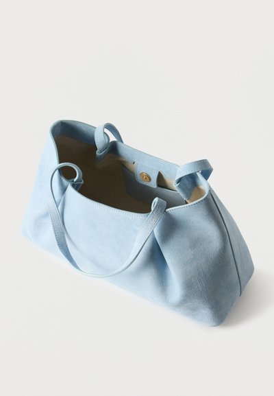 Τσάντα χειρός από γαλάζιο σουέτ με δύο λουριά και μαγνητικό κλείσιμο, εμφανιζόμενη ανοιχτή για να αποκαλύψει μπεζ εσωτερικό και μικρή εσωτερική τσέπη.