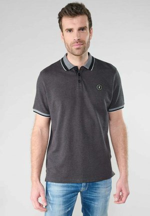 Polo shirt gris foncé avec un tissu texturé, col contrastant et accent de manches en noir et blanc, présentant un petit logo sur la poitrine.