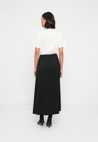 Jupe longue noire avec ceinture élastique, associée à un t-shirt blanc. Tissu lisse, coupe fluide, style minimaliste. Chaussures à talons hauts visibles.