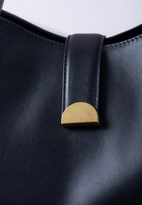 Black leather handbag featuring a rounded gold-toned metal clasp and a smooth texture, with contrasting stitching along the edges.