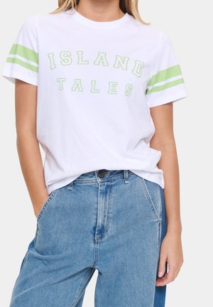 Kvinde iført en hvid t-shirt med grønne striber på ærmerne og grøn tekst "ISLAND TALES" kombineret med højtaljede blå jeans.