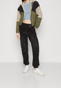 Färgblockerad jacka i oliv, beige och svart, parat med svarta cargobyxor med sidofickor och elastiska muddar. Vita sneakers.