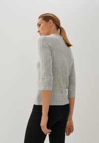 Schwarz-weißer strukturierter Oberteil mit taillierter Form, Dreiviertelärmeln und hohem Kragen, kombiniert mit schwarzen Hosen.