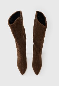 Cizme maro până la genunchi din material pufos, cu vârf ascuțit și fermoare laterale. Prezintă un finisaj texturat și o potrivire strânsă.