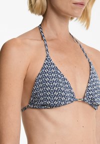 Tengerészeti kék és krémszínű mintás bikini top, háromszög alakú, vékony pántokkal és arany csattal elöl.