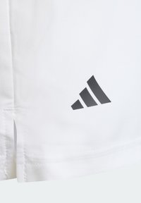 Camisa deportiva blanca de mangas cortas, con un logotipo triangular negro en la parte inferior izquierda, hecha de una tela suave y ligera.