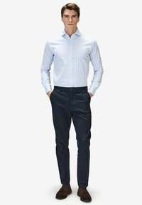 Vaaleansininen ja valkoinen raitapaita, tummansiniset housut ja ruskeat mokkakengät. Paidassa on klassinen kaulus ja pitkät hihat.