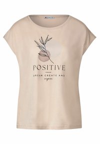 Béžové tričko, krátké rukávy, kulatý výstřih. Na přední straně je černý grafický motiv listu a text: „POZITIVNÍ SNY, TVOŘIT A INSPIRUJTE." Hladká textura.