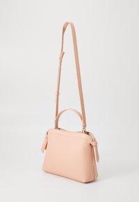 Persikofärgad läderhandväska med en texturerad yta, ett handtag upptill och en justerbar axelrem. Har guldfärgad hårdvara och tofsdetaljer.