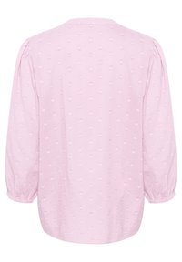 Blouse rose à manches longues avec un tissu texturé à petits motifs en forme de cœur, col rond et poignets élastiques. Fini lisse.