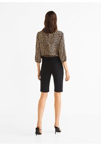 Blouse à imprimé léopard avec manches trois-quarts, associée à un short noir ajusté et des sandales à talons hauts.