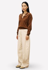 Pull en tricot marron avec un détail de col blanc, assorti à un pantalon beige à jambes larges avec des coutures latérales. Des chaussures décontractées complètent le look.