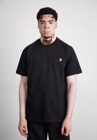 Black cotton t-shirt featuring a round neck and short sleeves, accented with a small yellow and red logo on the left chest.