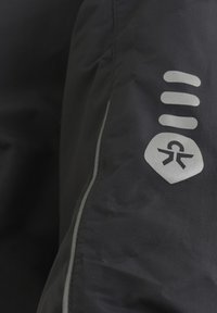 Svart jacka med en texturerad tyg, som har reflekterande kantband, en silverfärgad logo och stiliserade grafiska detaljer på ärmen.