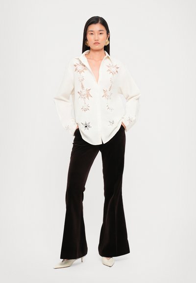 White button-up shirt with star embroidery, paired with black flared pants. Model wears beige pointed heels and statement earrings.