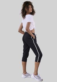 Zwarte cropped joggers met witte zijstrepen, elastische tailleband en losse fit. Gecombineerd met een witte geknoopte t-shirt en sportieve sneakers.