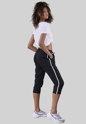 Black cropped joggers with white side stripes, elastic waistband, and relaxed fit. Paired with a white knotted t-shirt and sporty sneakers.