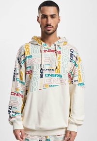 Hooded sweatshirt featuring multicolored "DNGRS" logos on the upper half, cream lower portion, and a textured fabric with ribbed cuffs.