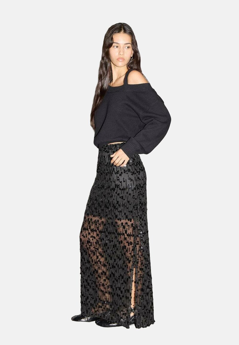 Jersey negro oversize con diseño de hombros descubiertos, combinado con una falda maxi negra de gasa con detalles de lentejuelas y aberturas laterales.
