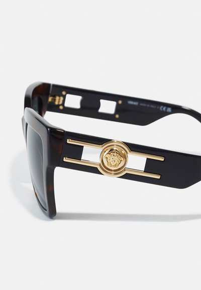 Schwarze Sonnenbrille mit Schildpatt-Akzenten, die ein markantes goldfarbenes Emblem in der Mitte des Bügels und ein rechteckiges Rahmendesign aufweist.