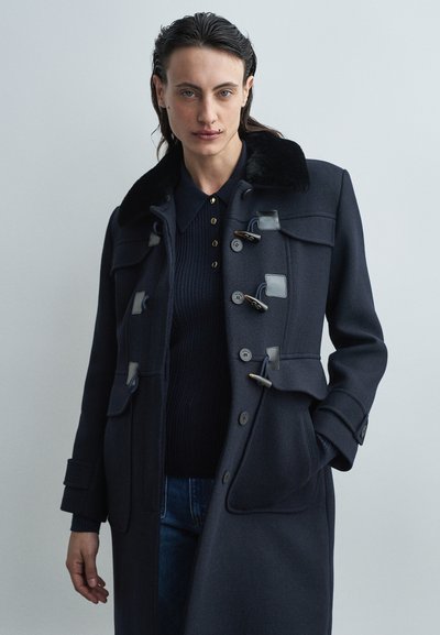 Marineblauer Wollmantel mit einem Kunstfellkragen, Knopf- und Toggle-Verschluss, Fronttaschen und gerippter Struktur darunter. Klassisches Design.