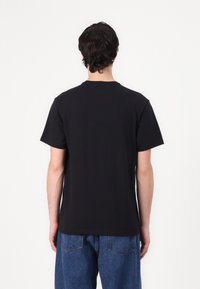 Black cotton t-shirt with short sleeves and a crew neck, featuring a minimalist design, viewed from the back, paired with blue denim jeans.