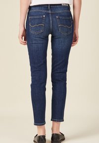 Tmavě modré džíny skinny s středním pasem, které mají dvě zadní kapsy s kontrastním prošíváním a ohrnutým lemem.