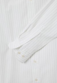 Camicia bianca con righe verticali blu. Collo button-down e polsini. Tessuto morbido con una texture liscia. Quattro bottoni visibili sul polsino.