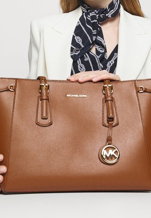 Bruine synthetische leren handtas met goudkleurige accenten, dubbele handvatten en een ronde MK-logo charme. Gladde textuur en gestructureerde vorm.