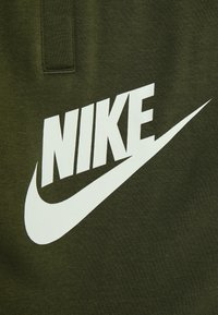 Olivově zelená látka s velkým bílým logem Nike a designem swoosh, hladká textura a čistý, výrazný grafický styl.