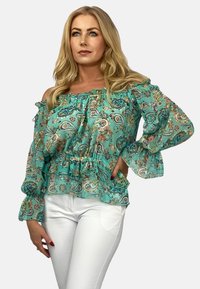 Błękitna bluzka na jedno ramię z falbaniastym dekoltem, długimi rękawami i kwiatowymi wzorami paisley, podkreślona dopasowaną talią.