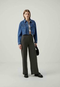 Avklippt blå denimjacka med nitar, i kombination med högmidjade ribbade olivgröna byxor och svarta kraftiga skor, samt en liten svart väska.