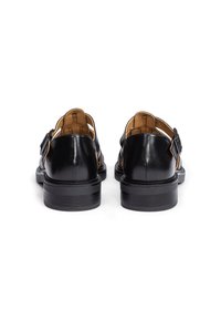Sandalias de cuero negro con suela plana, que presentan un diseño abierto y un detalle de hebilla. Textura suave con un acabado brillante.
