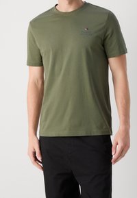 Camiseta de algodón verde oliva con escote redondo, mangas cortas y un pequeño logo bordado en el pecho izquierdo. Costuras planas y textura suave.