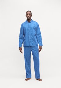 Set de pijama în carouri albastre, format dintr-o cămașă cu butoni și mâneci lungi și pantaloni asortați, realizat dintr-un material moale din bumbac, cu un croi lejer.