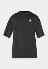 Schwarzes Baumwoll-T-Shirt mit kurzen Ärmeln, Rundhalsausschnitt, distressed Textur und gesticktem Logo auf der oberen linken Seite.