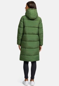 Long, puffy green coat with a hood, featuring horizontal quilted sections. Worn with dark pants and white sneakers, showing a straight cut design.