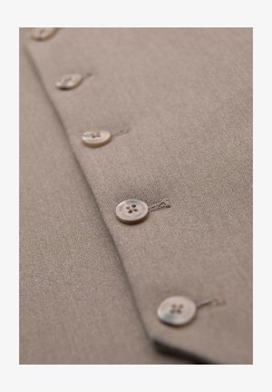 Beige stof met vier zichtbare beige knopen in een verticale rij genaaid, met het woord "OMBRE" in elke knop gegraveerd.