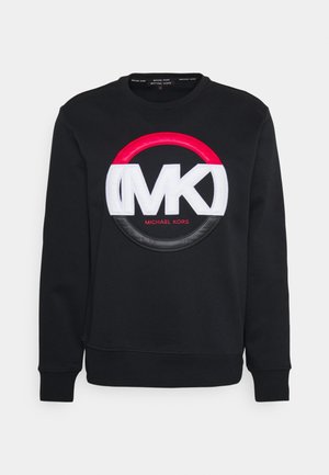 Sweatshirt noir à col rond avec grand logo MK blanc, détail cercle rouge et noir, et petit texte rouge "Michael Kors" centré sous le logo.