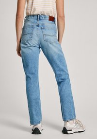 Jeans de mezclilla azul claro con una cintura alta, diseño de pierna recta y dos bolsillos traseros. Combinados con zapatillas deportivas blancas y una blusa a rayas.
