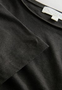 T-shirt in lino nero con vestibilità rilassata, dotata di scollo rotondo e texture morbida. Orlo e cuciture delle maniche visibili, senza motivi o grafiche.
