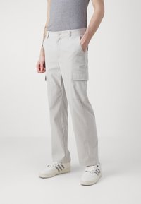 Pantalones cargo de color gris claro con un corte relajado, que cuentan con bolsillos laterales, pasadores para cinturón y cierre de botón en la parte delantera. Fabricados con un tejido duradero.