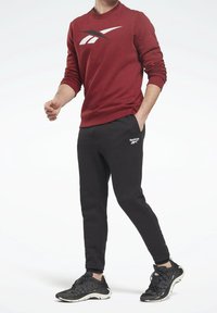 Sweat-shirt rouge avec un grand logo noir, associé à un pantalon de survêtement noir fuselé avec un logo de marque blanc. Des chaussures de sport noires complètent le look.