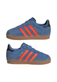 Blå ruskinn sneakers med oransje tre striper og logo, teksturert gummisåle, snøring design og svarte aksenter på hælen.