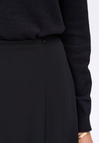 Zwarte trui gemaakt van breiwerk, gecombineerd met een zwarte rok met een gladde textuur en een knoopdetail op de tailleband.