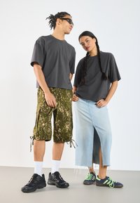 Šedé oversized trička, zelené maskáčové cargo šortky, světle modrá džínová sukně s bočním rozparkem, černé tenisky a bílé ponožky.
