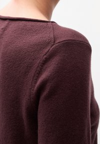 Gros plan sur le haut du dos et l'épaule d'une personne portant un pull en maille texturé de couleur violet foncé avec des détails de coutures visibles.